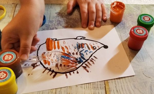 Na białej kartce papieru narysowany jest kontur jeża, na którym dziecko domalowuje wzór za pomocą widelca zamoczonego w farbie