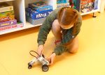 Dziewczynka włącza ustawionego na podłodze robota zbudowanego z klocków Lego Mindstorms