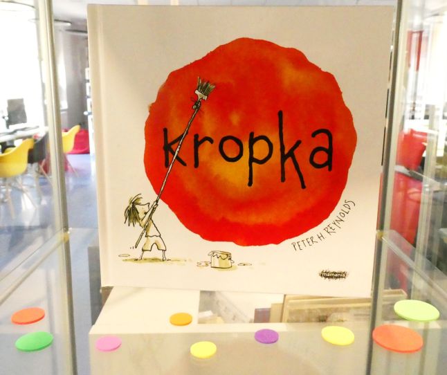 Okładka książki „Kropka” – na biały tle duża czerwona kropka, którą pędzlem maluje dziewczynka, bohaterka książki