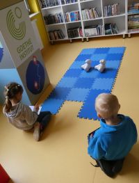 Chłopiec i dziewczynka siedzą na podłodze, bawiąc się robotami Photon z wykorzystaniem tabletów