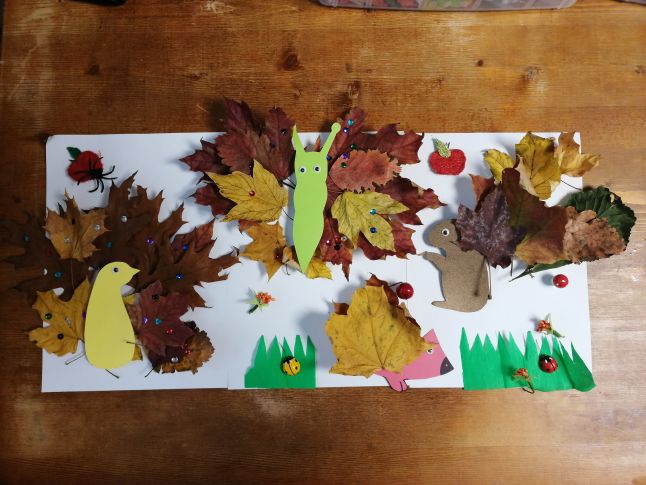 Praca plastyczna wykonana z kolorowych liści oraz papierowych szablonów, przedstawiająca pawia, motyla, wiewiórkę i jeża