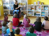 Grupa dzieci w wieku przedszkolnym ogląda ilustracje z książki o psach, które prezentuje bibliotekarka