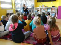 Grupa dzieci w wieku przedszkolnym słucha opowiadania czytanego przez bibliotekarkę