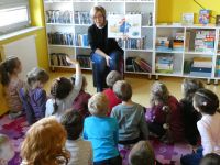 Grupa dzieci ogląda ilustracje do książki pt. „Pieski pana Kieszonki”, które czyta bibliotekarka