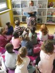 Grupa dzieci słucha opowiadania czytanego przez bibliotekarkę