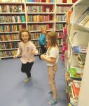 Dzieci szukają kredek ukrytych na półkach z książkami