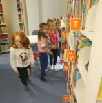 Dzieci szukają kredek ukrytych na półkach z książkami