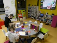 Chłopiec i dziewczynka siedzą przy stole i przygotowują prace plastyczne z kartonów oraz kolorowych arkuszy papieru