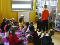 Chłopiec pokazuje grupie przedszkolaków ilustracje w książce, którą trzyma bibliotekarka