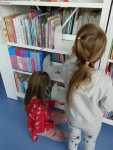 Dwie dziewczynki szukają obrazków ukrytych na regałach z książkami
