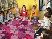 Przedszkolaki siedzą na dywanie w półkolu. Przed sobą mają kolorowe obrazki.