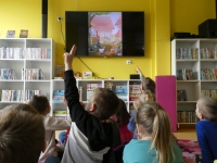 Przedszkolaki oglądają na ekranie telewizora ilustrację z książki