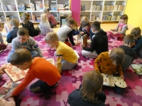Dzieci oglądają ilustracje w książkach, siedząc na dywanie