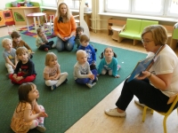 Grupa dzieci siedzi na dywanie i słucha opowiadania czytanego przez bibliotekarkę