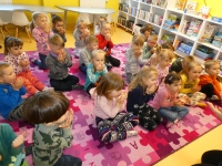 Przedszkolaki siedzą na dywanie i dmuchają w złożone w kształt miseczki dłonie
