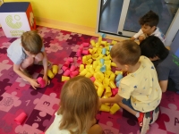 Grupa dzieci zbiera kolorowe plastikowe kubeczki rozsypane na podłodze